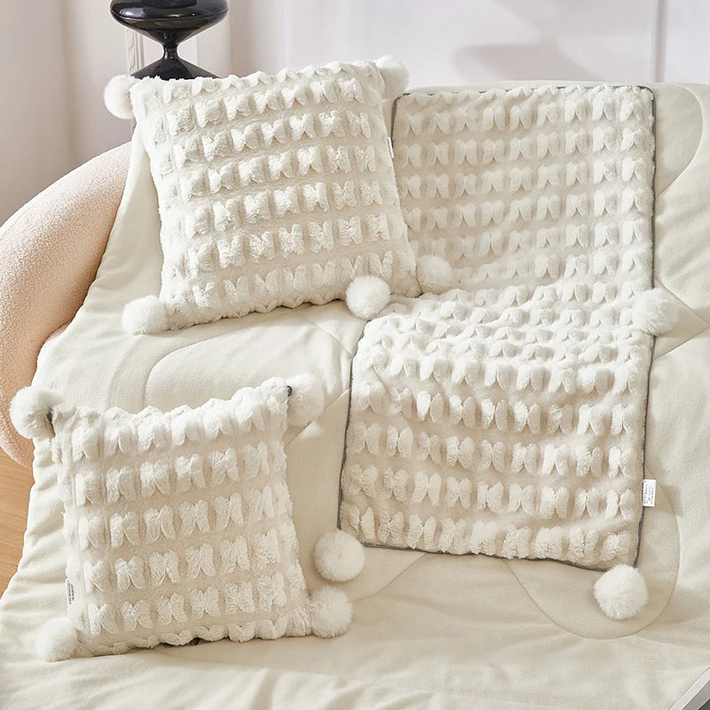 Cream plush throw pillow with waffle texture, pom-pom trim, and attached blanket cover